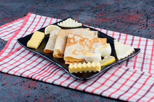 Planche de petit-déjeuner avec crêpes, fromage, citron et œufs.