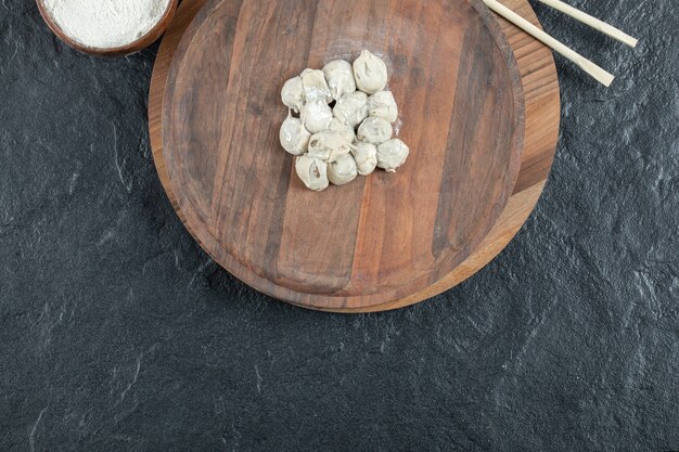 Une planche ronde en bois avec des boulettes non cuites et de la farine.