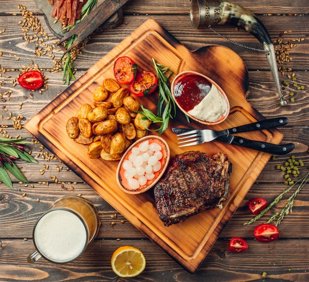 Planche à steak avec viande, pommes de terre et sauces.