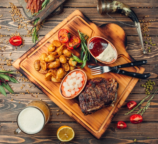 Planche à steak avec viande, pommes de terre et sauces.