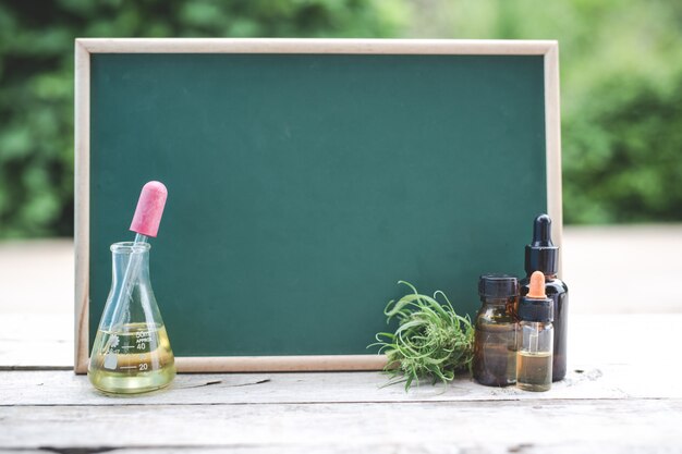 Sur le plancher de bois, il y a de l’huile de chanvre, une feuille de chanvre et le tableau vert est vide pour mettre du texte.