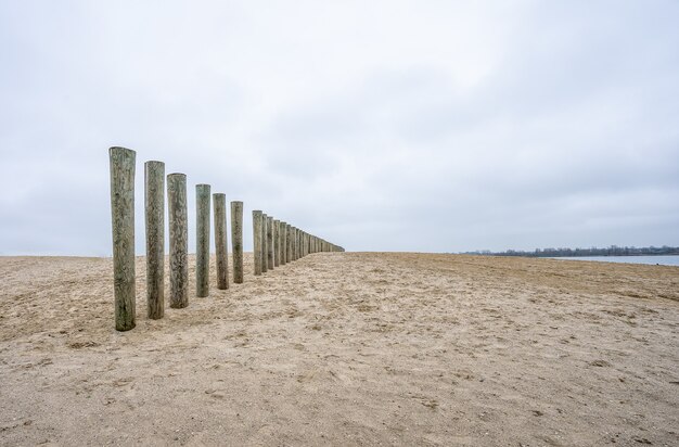 Planches de bois verticales d'un pont inachevé sur la plage sous un ciel nuageux
