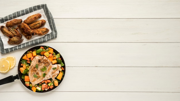 Photo gratuite plat avec des ailes de poulet et poêle de légumes sur le bureau en bois