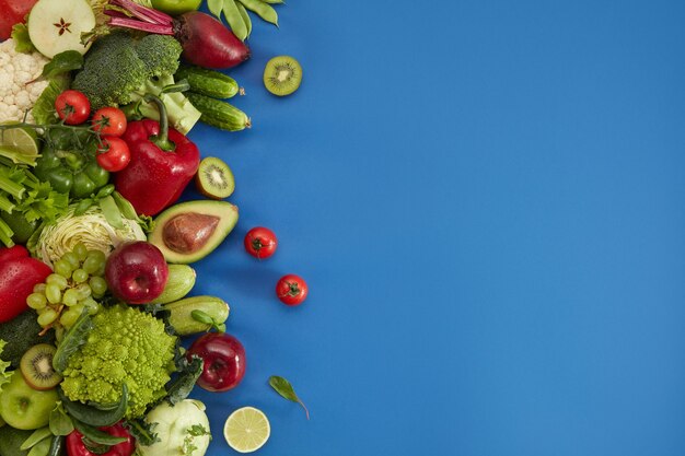 Plat d'aliments sains sur fond bleu. Ensemble sain comprenant des légumes et des fruits. Raisin, pomme, kiwi, poivre, citron vert, chou, courgette, pamplemousse, avocat. Bonne nutrition ou menu végétarien.