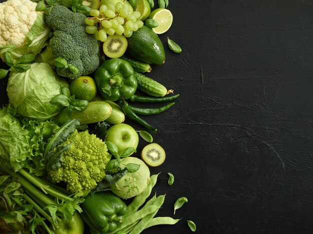 Plat d'aliments sains sur fond de pierre noire. Ensemble sain comprenant des légumes et des fruits. Raisin, pomme, kiwi, poivre, citron vert, chou, courgette, pamplemousse. Bonne nutrition ou menu végétarien.