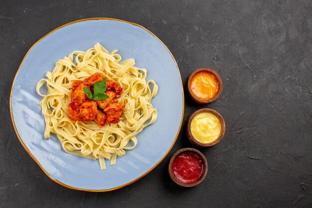 Plat vue de dessus avec sauces pâtes appétissantes avec sauce et viande dans l'assiette à côté des trois types de sauces sur la table sombre