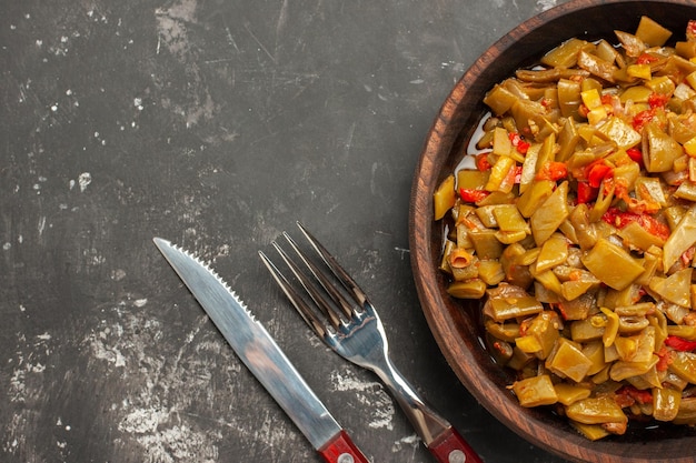 Photo gratuite plat de vue en gros plan sur la plaque de table des haricots verts et des tomates appétissants à côté de la fourchette et du couteau sur la table sombre