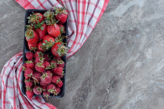 Plateau de baies juteuses avec fraises et framboises sur marbre.