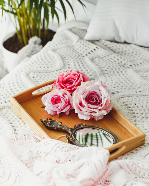 Plateau en bois avec miroir et roses roses sur une couverture tricotée