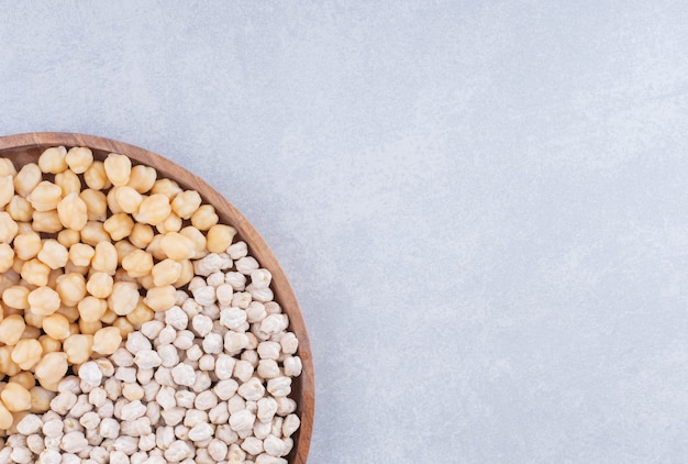 Plateau en bois avec des portions à moitié remplies de pois chiches crus et cuits sur une surface en marbre