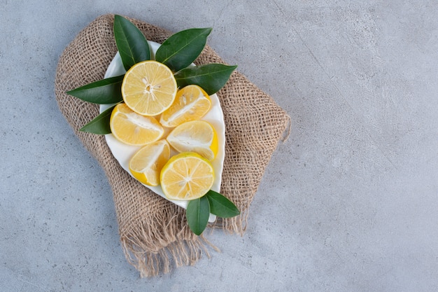 Un plateau de citrons tranchés sur un morceau de tissu sur fond de marbre.