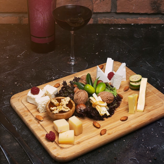 Plateau de fromages avec différents fromages, raisins, noix, miel, pain et dates sur du bois rustique. sur une planche de bois sombre avec une bouteille de vin et un verre de vin