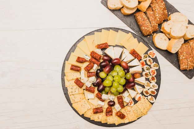 Plateau de fromages avec des raisins; saucisses fumées et pain