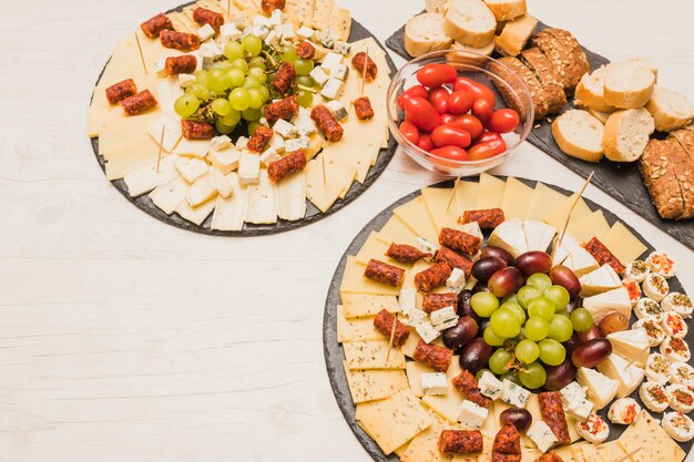 Plateau de fromages servi avec des tomates, des tranches de pain et des saucisses fumées sur une table en bois