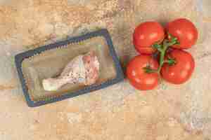 Photo gratuite un plateau noir avec cuisse de poulet cru et tomates