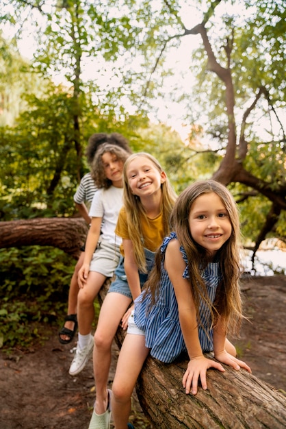 Photo gratuite plein coup d'enfants souriants assis sur une bûche