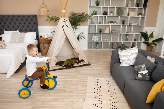 Plein coup heureux enfant faisant du tricycle à l'intérieur