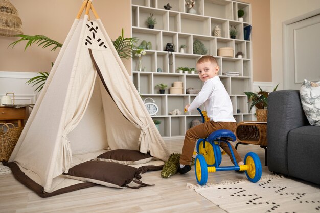 Plein coup heureux enfant faisant du tricycle à l'intérieur