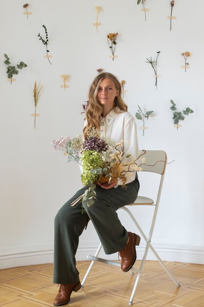 Plein coup jeune femme assise sur une chaise avec des fleurs