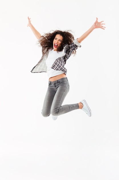 Pleine longueur Cheerful curly woman jumping et en regardant loin sur le mur blanc