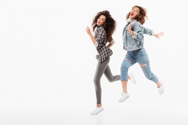 Pleine longueur deux filles espiègles courir ensemble sur un mur blanc