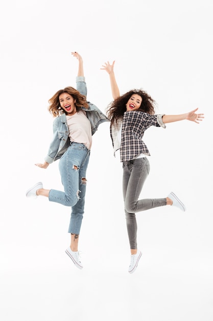 Pleine longueur deux filles joyeuses se réjouit et saute par-dessus le mur blanc