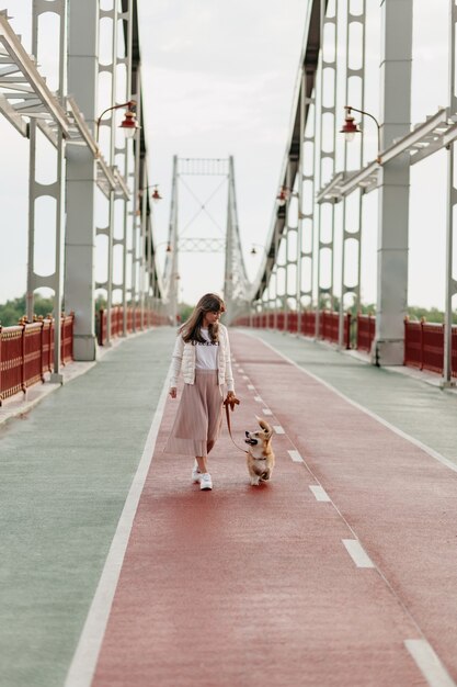 Pleine longueur de femme marchant dans un pont lumineux marchant avec corgi