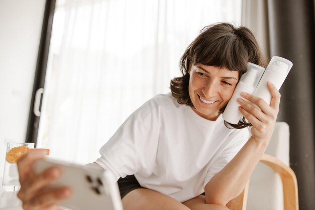 Pleine vue de femme souriante avec lotion faisant selfie