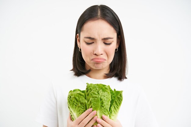 Pleurer femme tenant des légumes assis sur le régime alimentaire et manger du chou au lieu de la malbouffe blanc backgro