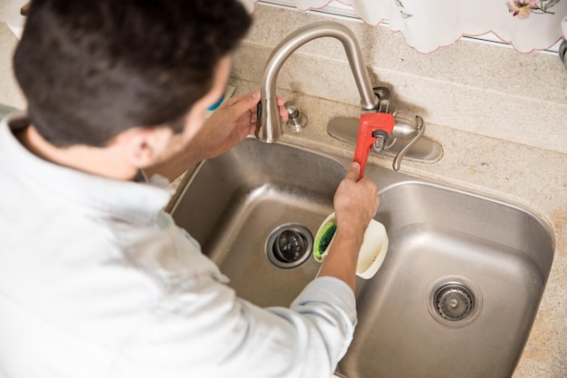 Plombier mâle utilisant une clé pour serrer un robinet d'eau dans une cuisine, vu de près