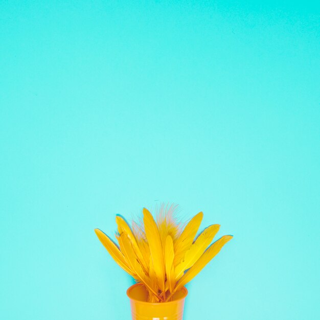 Plume jaune dans le verre jetable sur fond turquoise