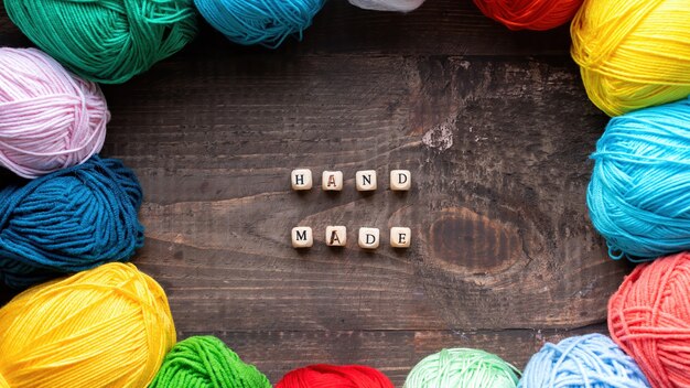 Plusieurs boules colorées de fil avec des lettres en bois composant des mots faits à la main. Vue de dessus