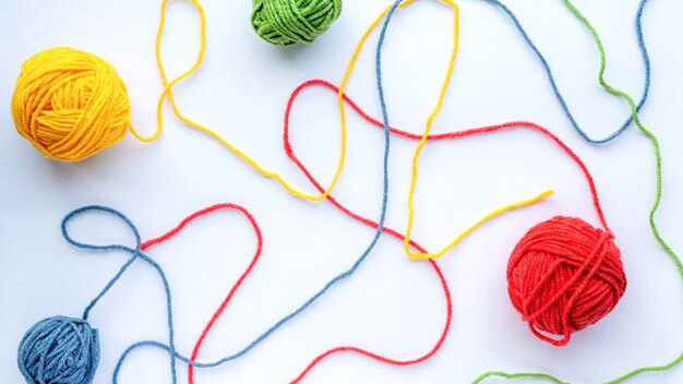 Plusieurs boules de fil partiellement non enroulées colorées sur un papier blanc. Vue de dessus