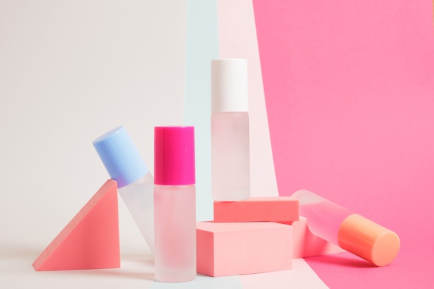 Plusieurs bouteilles de parfum de différentes couleurs sur un fond coloré et lumineux, des maquettes de bouteilles de parfum sur des supports géométriques roses