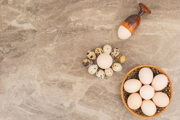 Plusieurs œufs sur le panier avec des œufs de caille dans la surface en marbre