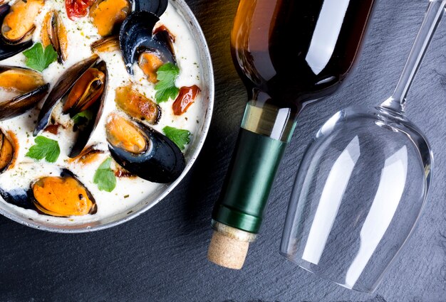 Poêle plate avec moules à la sauce blanche et bouteille de vin