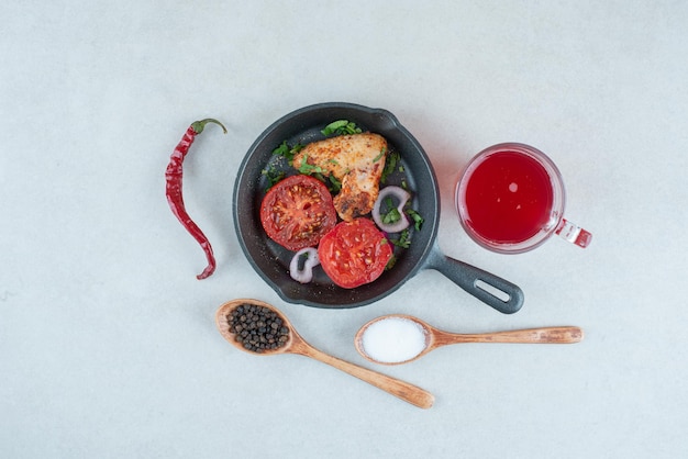 Une poêle sombre avec des tranches de tomates frites et du poulet sur un tableau blanc.