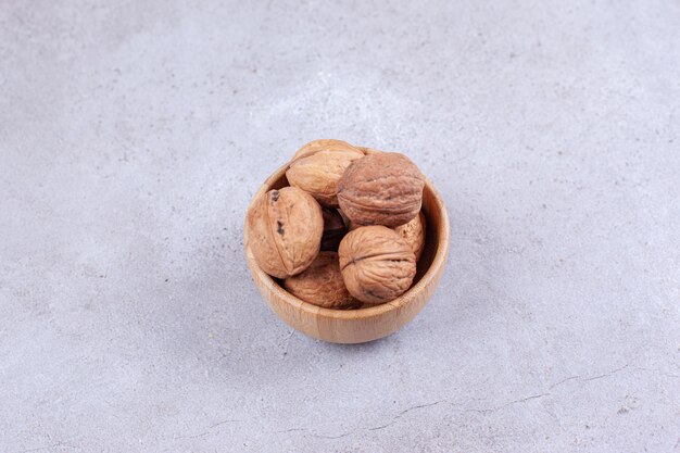 Une poignée de noix empilées dans un bol en bois sur une surface en marbre