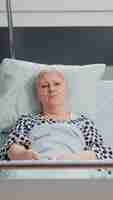 Photo gratuite point de vue d'une femme âgée malade parlant en appel vidéo pour une communication à distance, allongée dans un lit d'hôpital. patient senior avec tube à oxygène utilisant une conférence en ligne et regardant la caméra
