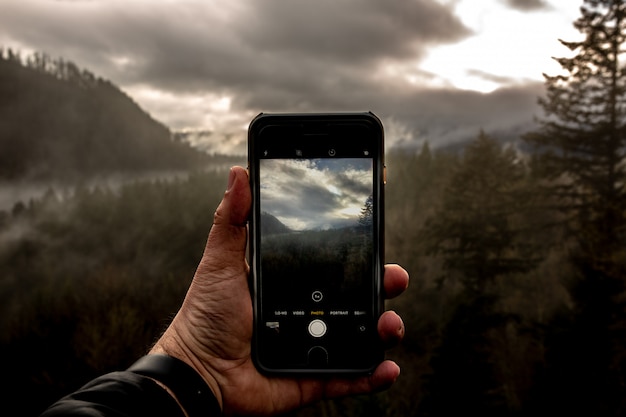 Photo gratuite point de vue d'un homme tenant un smartphone et prenant une photo d'un beau paysage