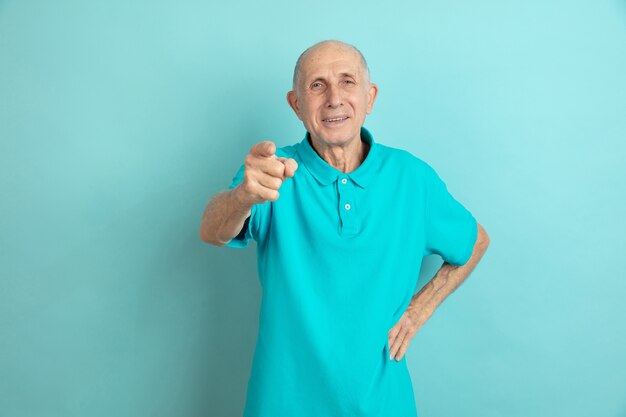 Pointant, vous choisissant. Portrait d'homme senior caucasien sur studio bleu.