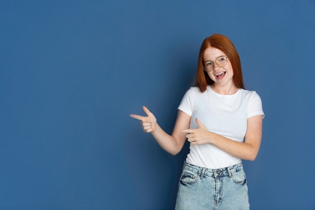 Pointer, choisir. Portrait de jeune fille caucasienne sur mur bleu.