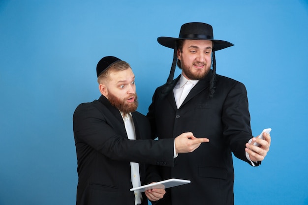 Photo gratuite pointer, choisir. portrait d'un jeune homme juif orthodoxe isolé sur mur bleu. pourim, affaires, festival, vacances, célébration pessa'h ou pâque, judaïsme, concept de religion.