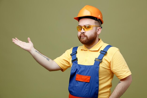 Points confiants à côté jeune constructeur homme en uniforme isolé sur fond vert