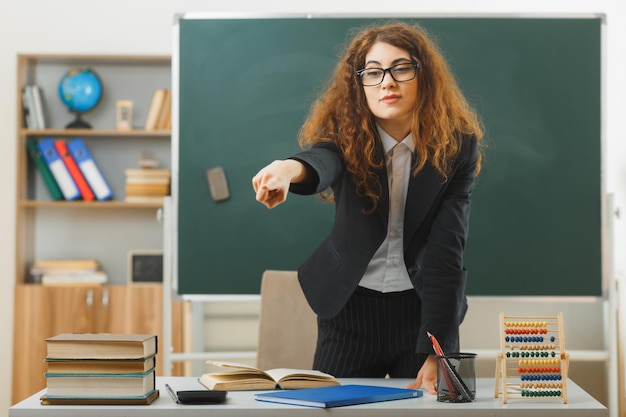 points confiants sur le côté jeune enseignante debout devant le tableau noir dans la salle de classe