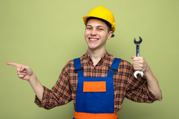 Des points souriants sur le côté du jeune constructeur masculin en uniforme tenant une clé à fourche