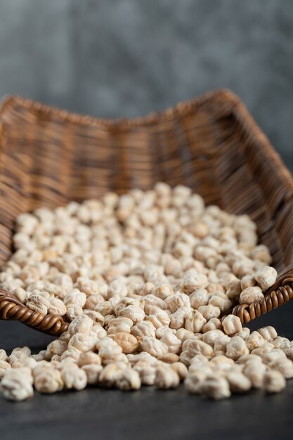 Pois blancs secs entiers dans un panier en osier sur fond noir.