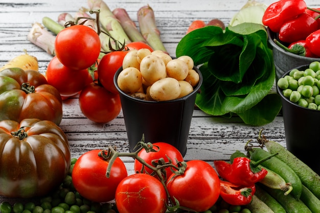 Pois et pommes de terre aux poivrons, tomates, asperges, bok choy, gousses vertes, carottes en mini seaux sur mur en bois, high angle view.