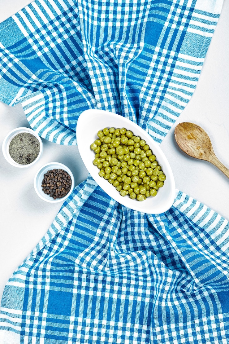 Photo gratuit pois verts bouillis dans un bol blanc avec des épices, une cuillère et une nappe.