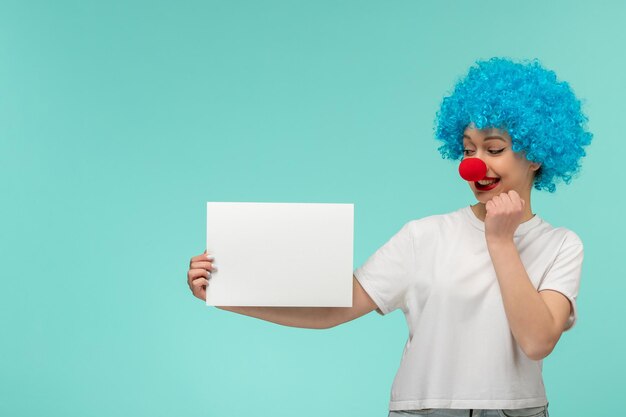 Poisson d'avril fille excitée tenant du papier avec un nez rouge dans un costume de clown cheveux bleus